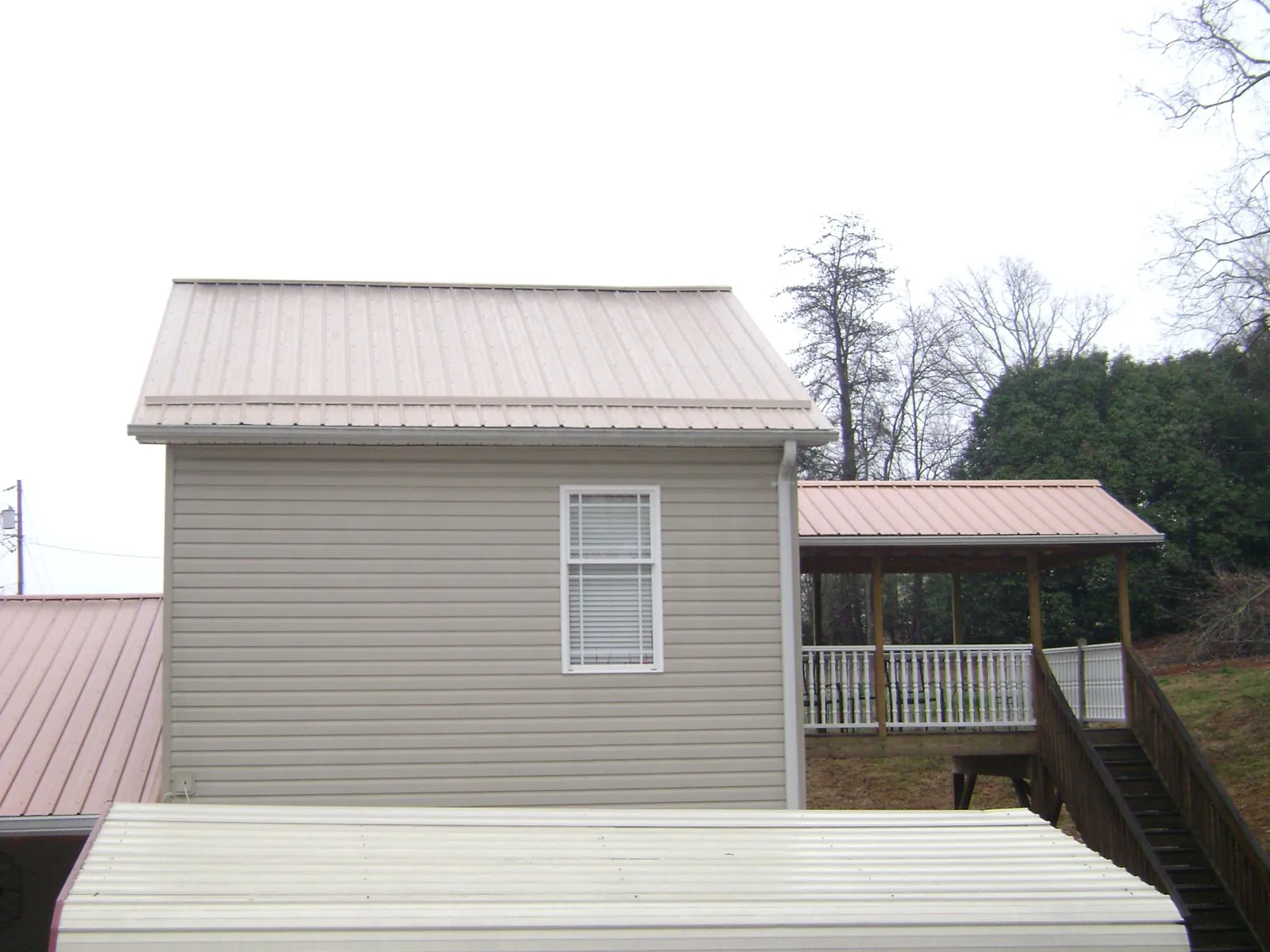 Tan metal roofs on a two story addition and attached porch, from a Roof Replacement job in Madison